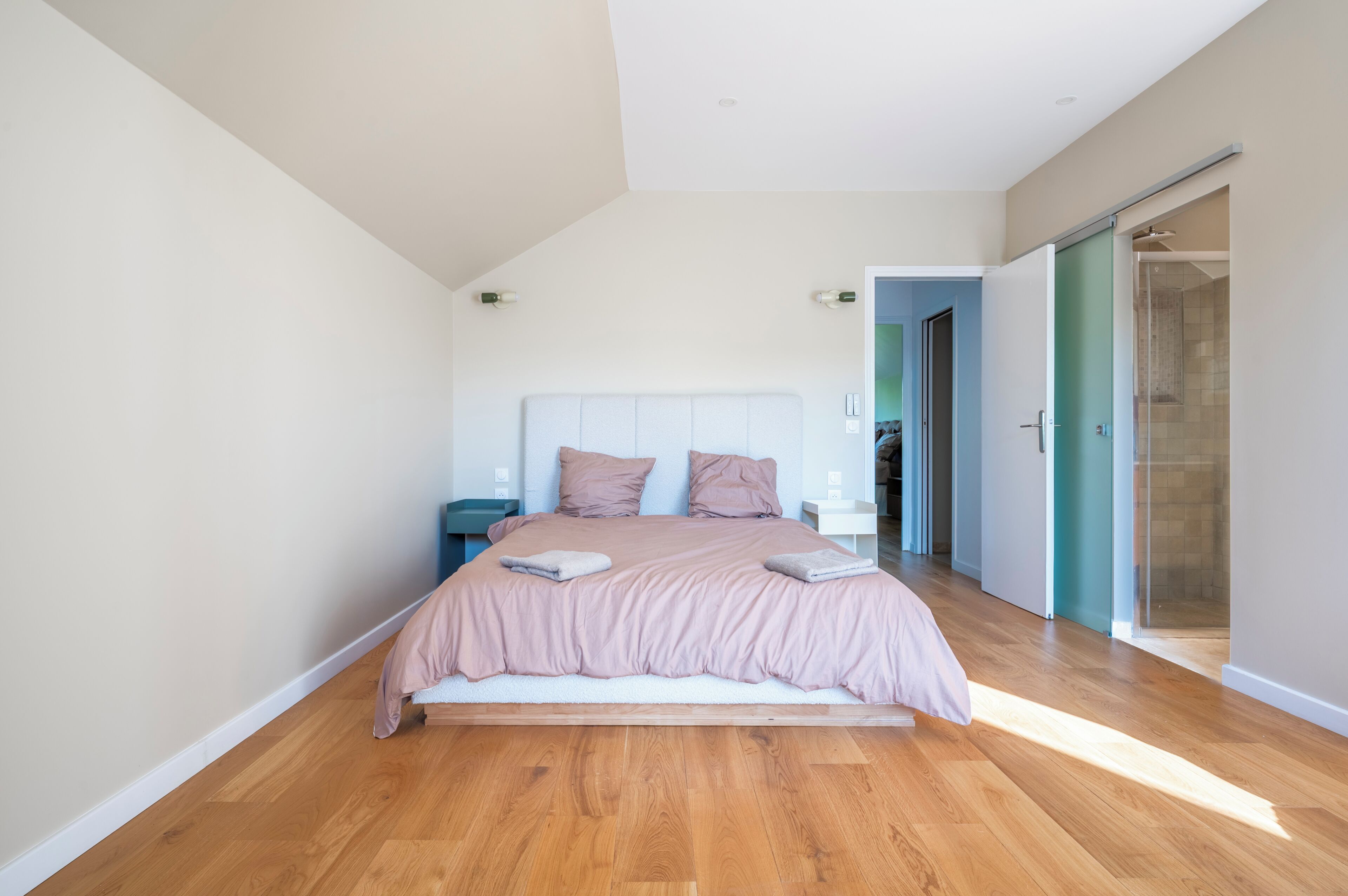 A modern bedroom with a large bed, wooden flooring, and a glass shower door.