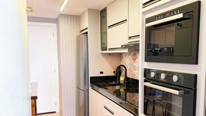 A modern kitchen with a built-in oven, a stovetop, and a refrigerator. - ASA Coral Sea Gravata 2BR (Navegantes)