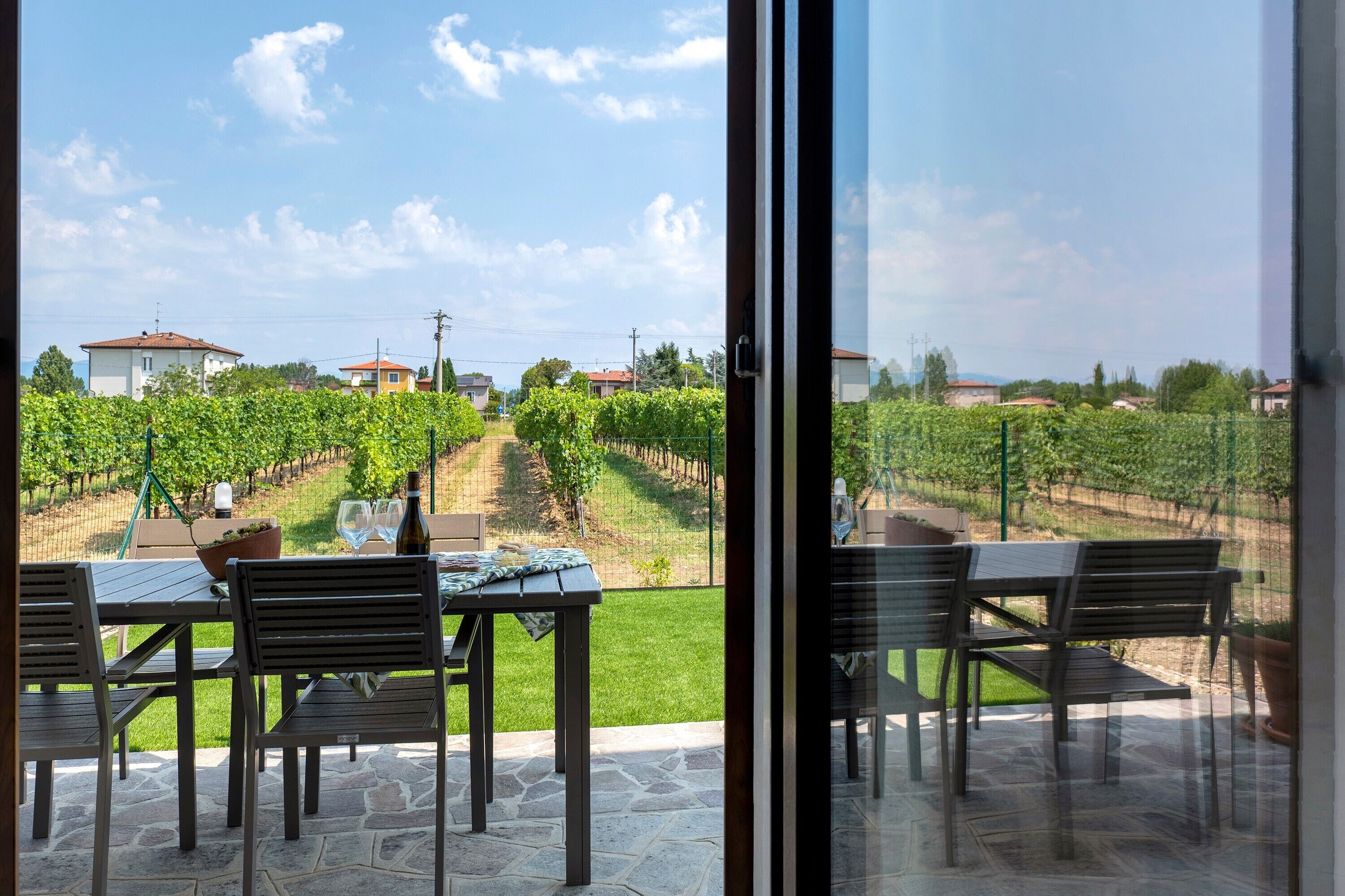 A patio with a table and chairs, overlooking a vineyard.