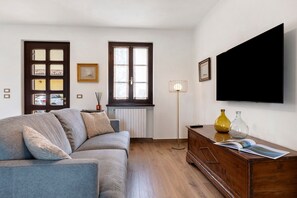 A living room with a sofa, a wooden cabinet, a floor lamp, and a flat-screen TV mounted on the wall.