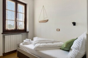 A bedroom with a bed, a window, a radiator, and a wall-mounted light fixture.