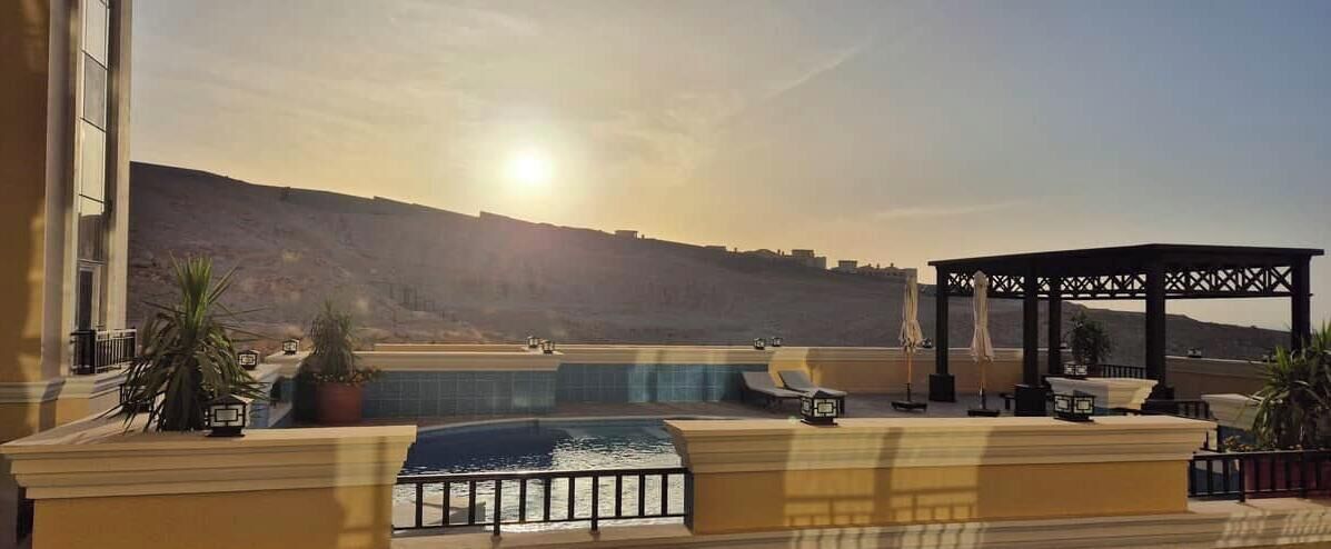 A rooftop pool area with a pergola and lounge chairs, overlooking a mountainous landscape.