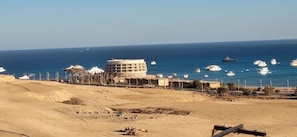Eine Küstenlandschaft mit sandigem Strand, einem Gebäude mit flachem Dach und mehreren Booten im Wasser.