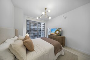 Ein Schlafzimmer mit einem Bett, einem Fernseher und einem Fenster mit Blick auf Palmen.