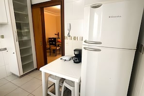 Une cuisine compacte avec un réfrigérateur blanc, une machine à café et une balance sur le plan de travail.