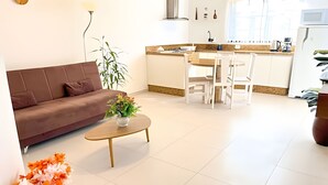 Una sala de estar moderna con un sofá, una mesita de centro con una planta, y una zona de cocina con una mesa de comedor y sillas.