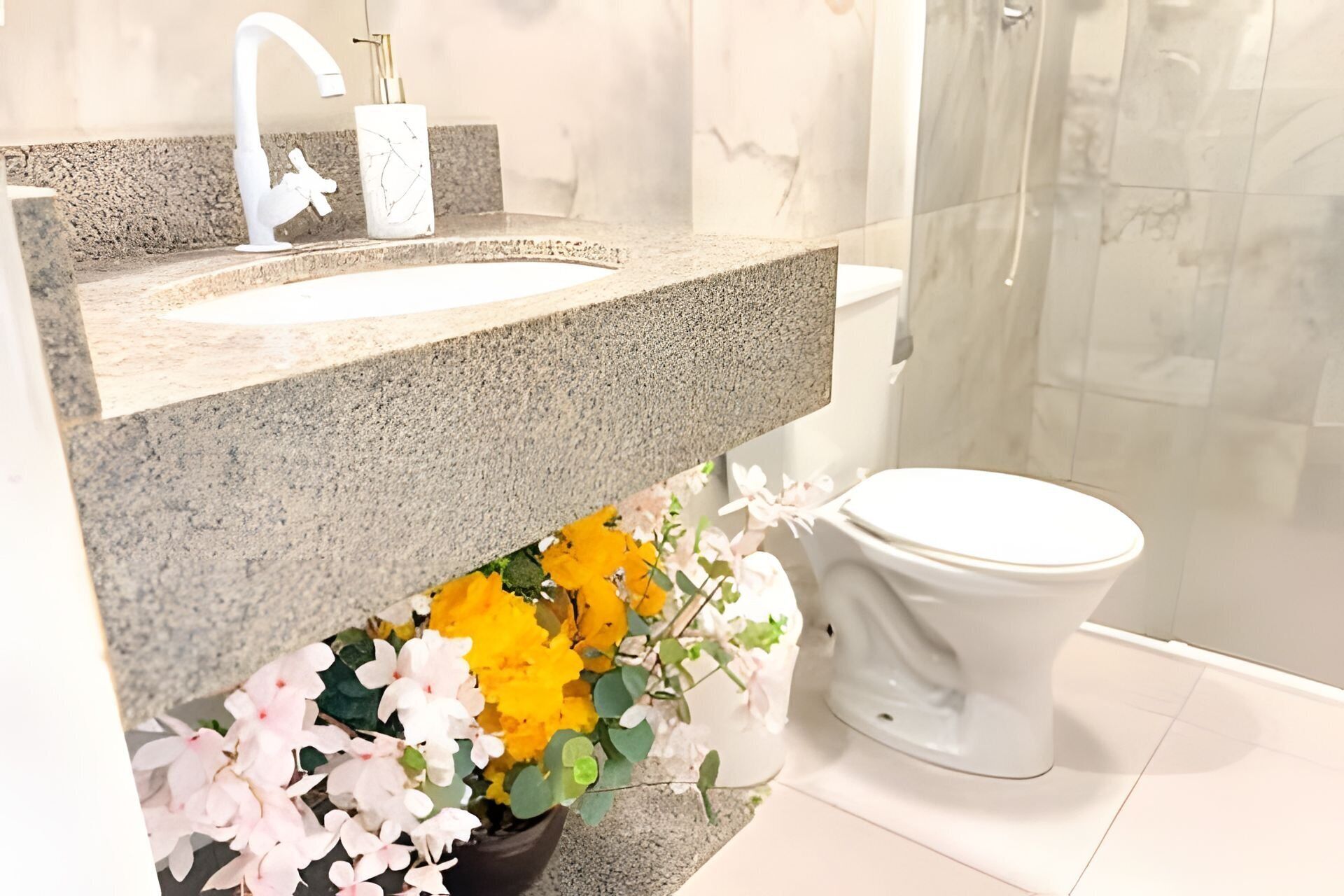 A bathroom with a granite countertop, a white sink, a toilet, and a shower area.