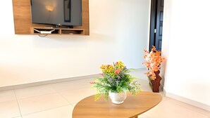 Una habitación con un mueble bajo de televisión de madera, una pequeña mesa con planta en maceta y una puerta con un arreglo floral decorativo.