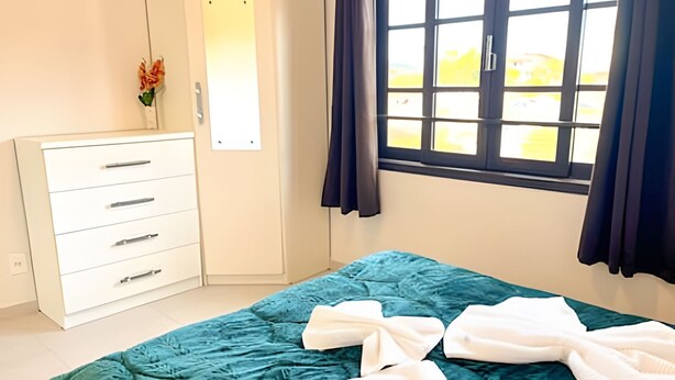 Un dormitorio con cama, cómoda, espejo y ventana con cortinas.