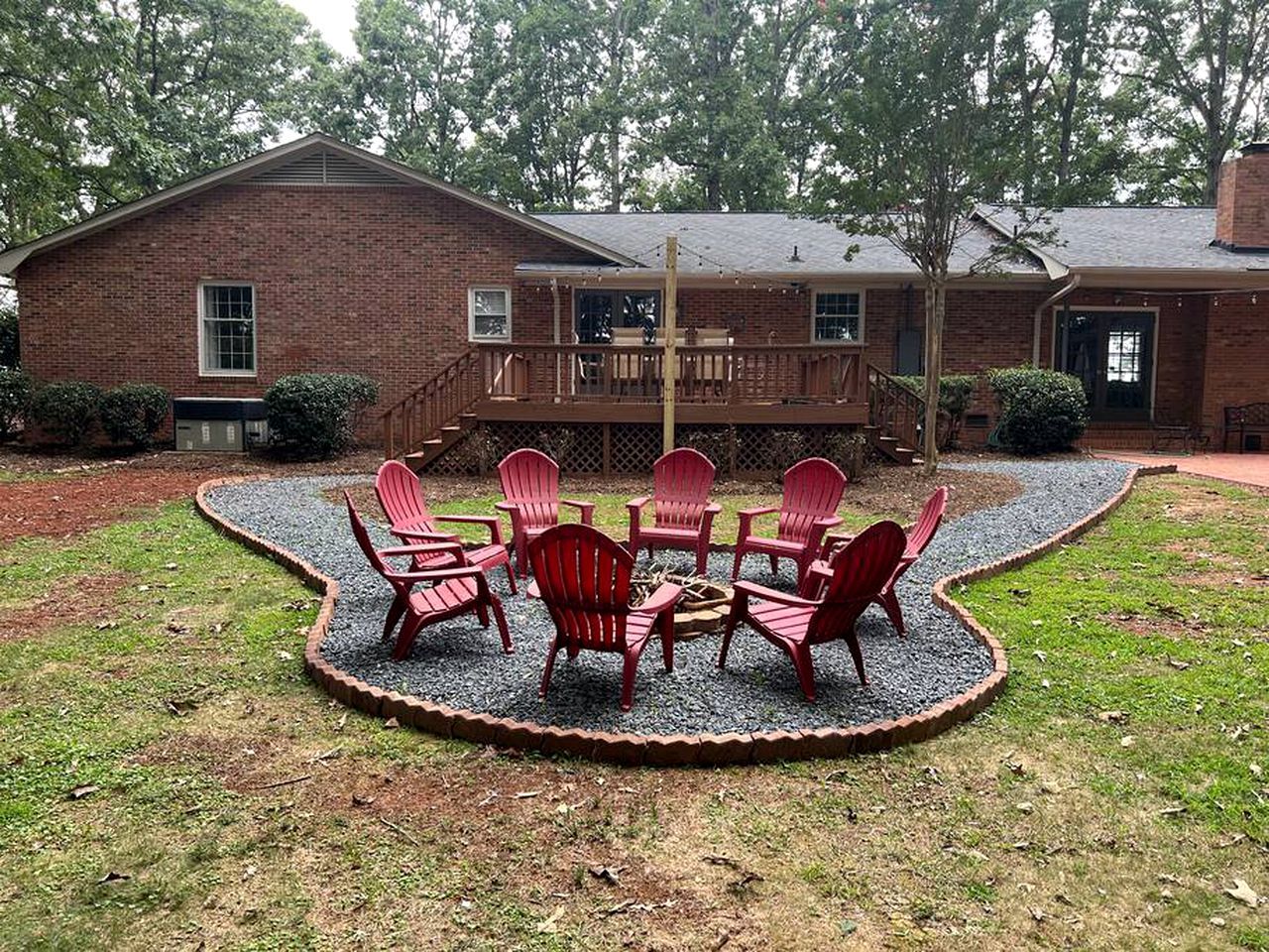 A brick house with a deck and a fire pit surrounded by red chairs.