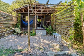 Una cabaña de madera con una hamaca, una pequeña zona de estar al aire libre y suelo de grava.