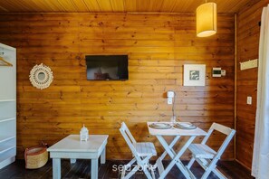 A cozy wooden cabin interior with a television, framed artwork, and a table set for dining. - Charming and Well-equipped Chalet Rel0002 (Imbituba)