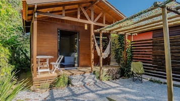 Uma cabana de madeira com varanda, uma rede e uma mesa pequena.