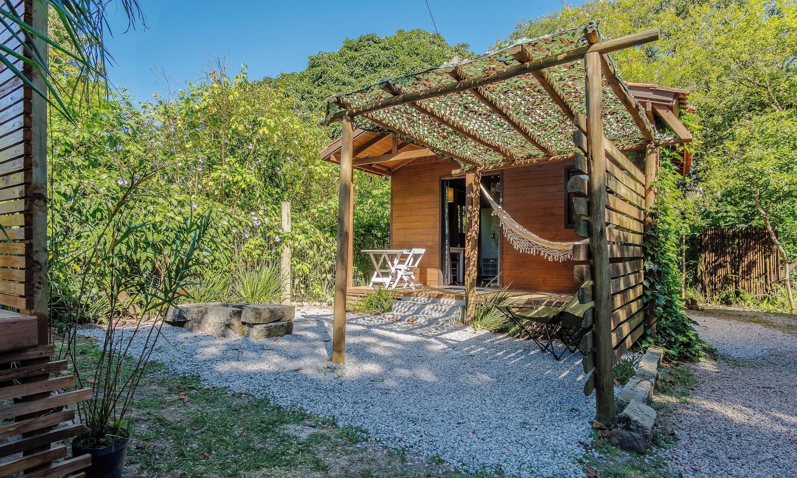 Una cabaña de madera con porche, rodeada de grava y follaje.