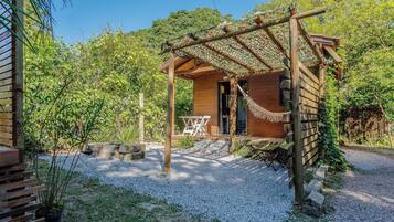 A wooden cabin with a porch, surrounded by gravel and greenery.