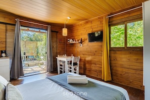 A wooden cabin room with a bed, a table, and a TV. - Complete Chalet in Imbituba Rel0001 (Imbituba)