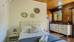 Un dormitorio con cama, mesita de noche, lámpara, adornos en la pared y vistas a la cocina.