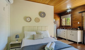 A bedroom with a bed, bedside table, lamp, and a view of the kitchen. - Complete Chalet in Imbituba Rel0001 (Imbituba)