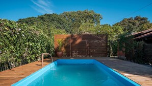 Una piscina rectangular con un muelle de madera que la rodea, una valla de madera y abundante vegetación al fondo.