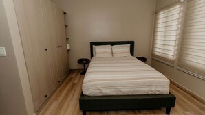 Ein Schlafzimmer mit einem Bett, einem Kleiderschrank, einem Nachttisch und einem Fenster mit Jalousien.