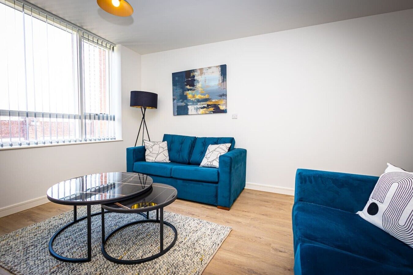 Una sala de estar moderna con un sofá azul, una mesa de centro redonda y un cuadro en la pared.