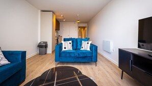 A modern living room with a blue sofa, a black coffee table, and a TV on a cabinet. - Birmingham City Retreat No 126 (Birmingham)