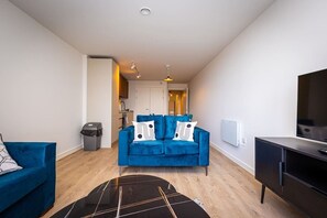 A modern living room with a blue sofa, a black coffee table, and a TV on a cabinet. - Birmingham City Retreat No 126 (Birmingham)