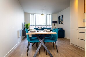A modern dining area with a wooden table, teal chairs, and a black floor lamp. - Birmingham City Retreat No 126 (Birmingham)
