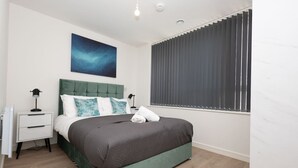 A bedroom with a bed, a nightstand, a lamp, a window with blinds, and a wall-mounted artwork. - Birmingham City Retreat No 126 (Birmingham)
