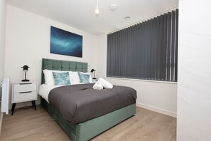 A bedroom with a bed, a nightstand, a lamp, a window with blinds, and a wall-mounted artwork. - Birmingham City Retreat No 126 (Birmingham)