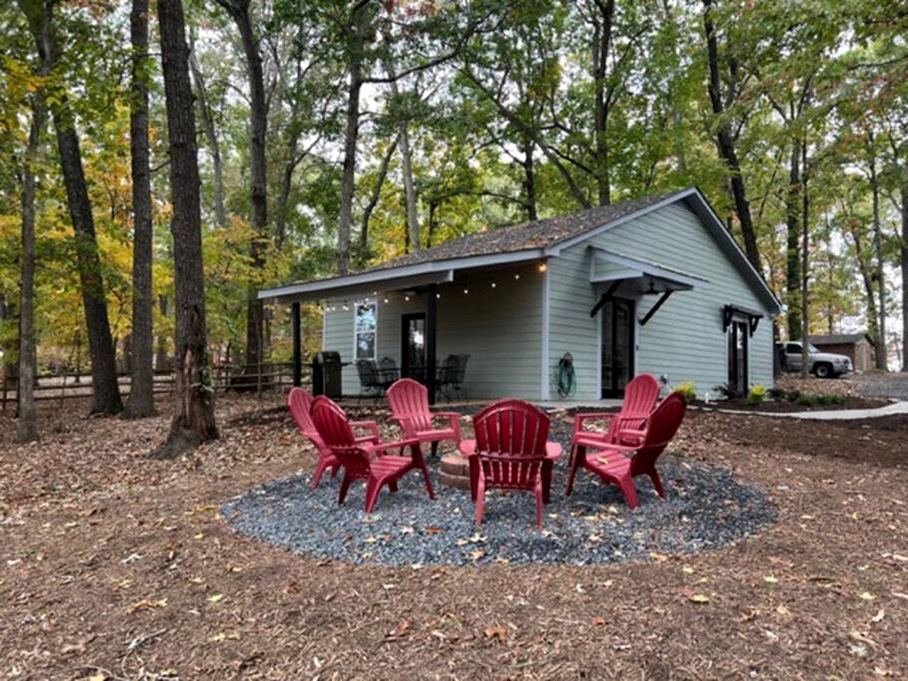 A house with a porch, surrounded by trees, and a seating area with chairs.
