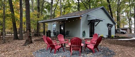 A house with a porch, surrounded by trees, and a seating area with chairs.