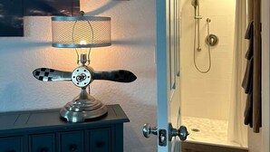 Quarto com luminária de estilo vintage, área de chuveiro e quadro fixado na parede.