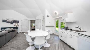 A modern kitchen with white cabinetry, a dining table with white chairs, and a grey sofa.