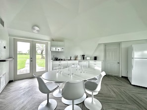 Una cocina moderna con una mesa de comedor redonda y sillas, armarios blancos y vistas a través de la puerta de cristal.