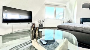 Uma sala de estar moderna com televisão de tela plana, uma mesa de centro de vidro, um sofá e uma cama.