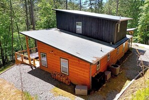 En etagehøj hytte med ståltag, trævægge og en grusindkørsel.