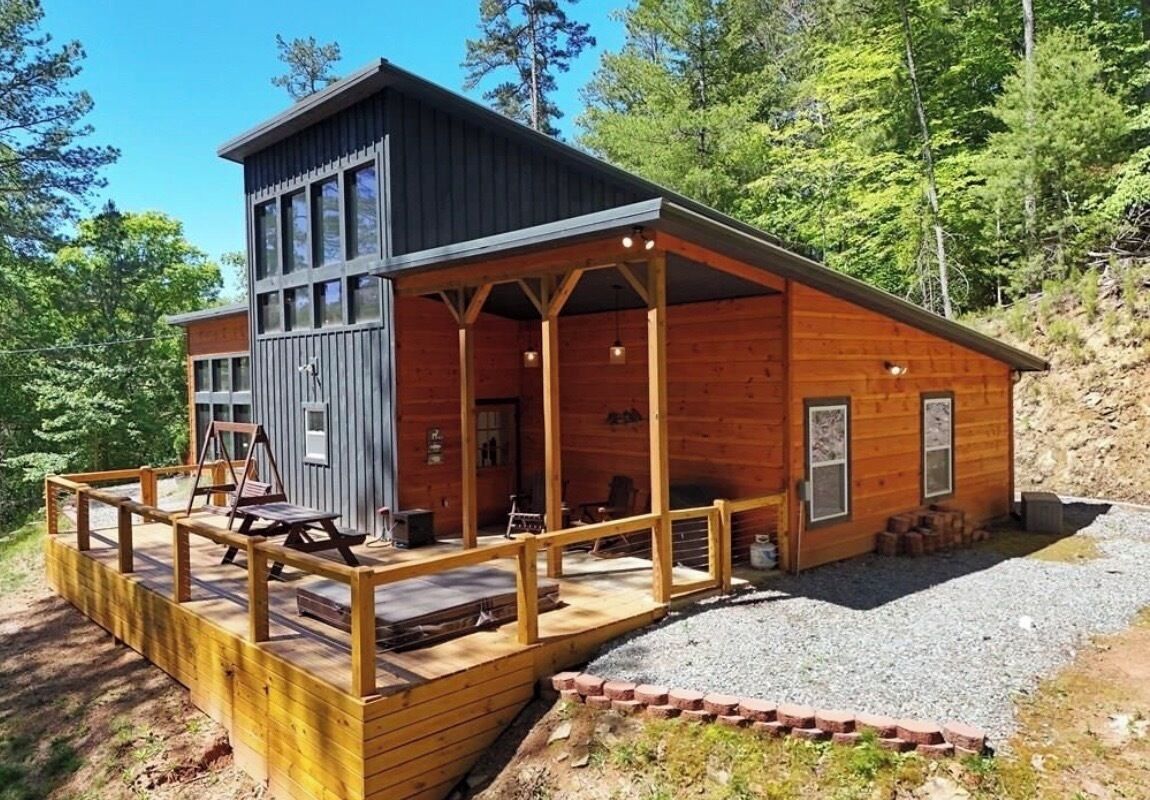 A two-story wooden cabin with a deck, a covered porch, and a gravel driveway.