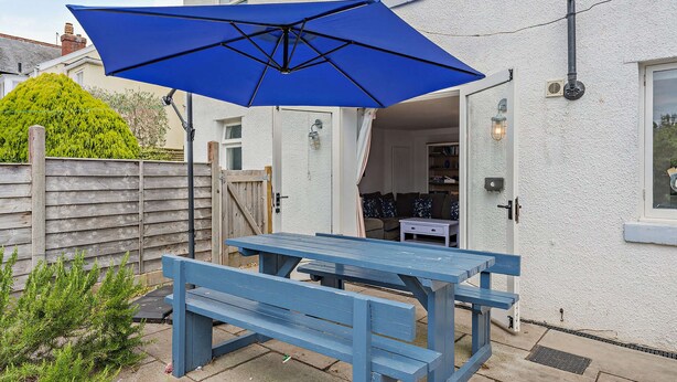 A blue picnic table with an umbrella, a wooden fence, and a house with a white exterior. - Host & Stay | The Hidden House (Dawlish)
