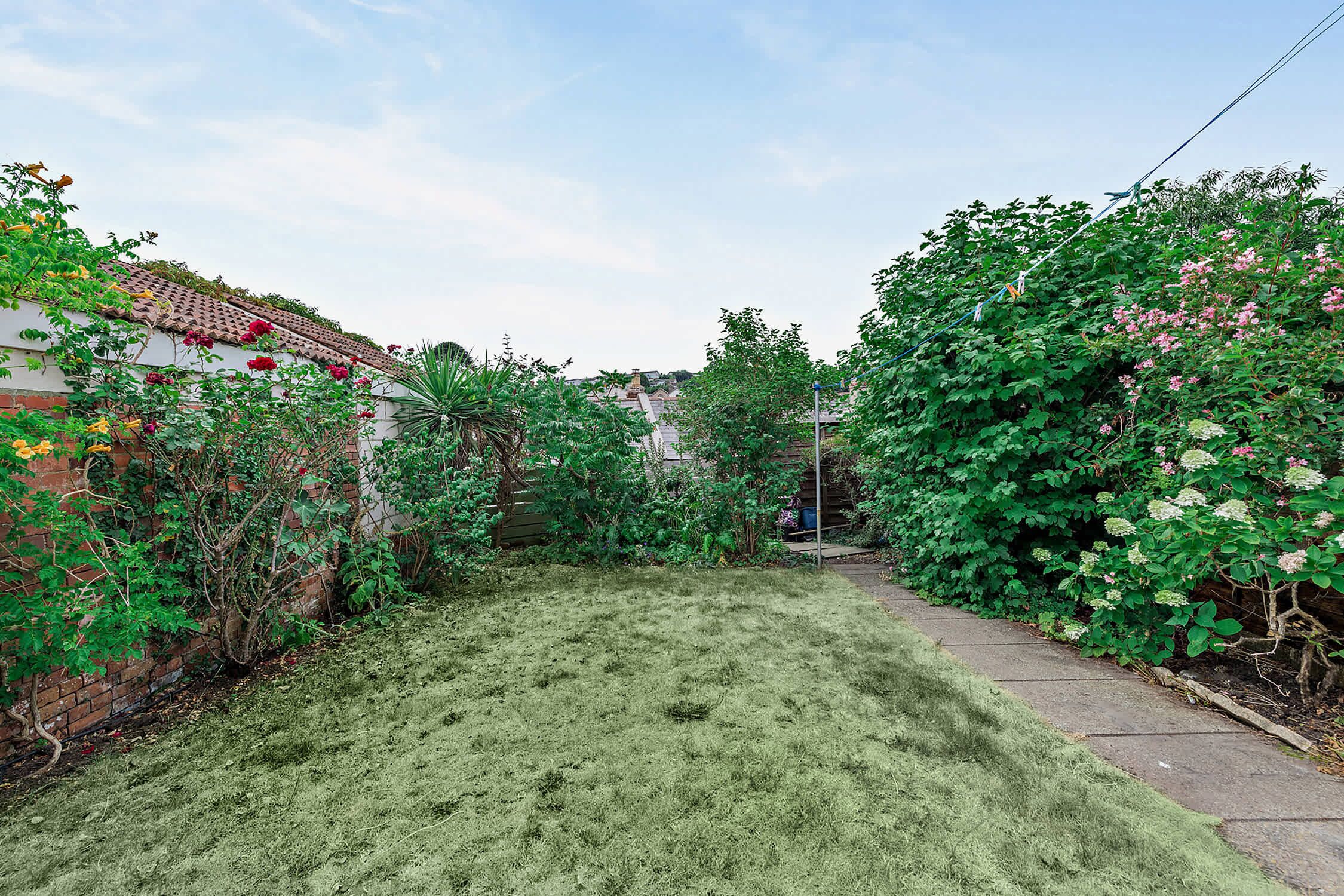Un jardin résidentiel avec une pelouse, un mur en briques et diverses plantes à fleurs.