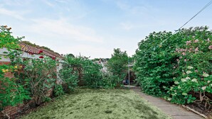 A residential garden with a lawn, a brick wall, and various flowering plants. - Host & Stay | The Hidden House (Dawlish)