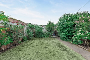 A residential garden with a lawn, a brick wall, and various flowering plants. - Host & Stay | The Hidden House (Dawlish)