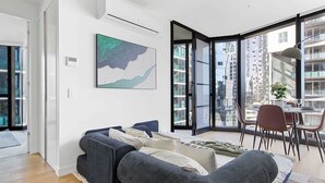 A modern living room with a dark grey sofa, a large abstract painting, and a dining area with a table and chairs. - Luxury CBD Stay, Pool, Spa & City Views (Melbourne)