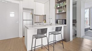 A modern kitchen with a central island, bar stools, a refrigerator, and a microwave. - Luxury CBD Stay, Pool, Spa & City Views (Melbourne)