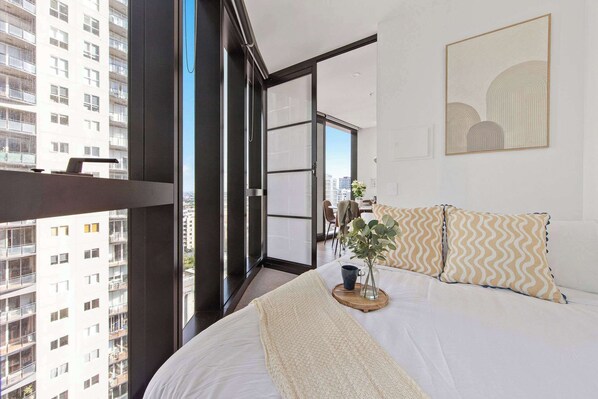 A modern bedroom with a large bed, a view of the city through floor-to-ceiling windows, and a cityscape visible from the balcony. - Luxury CBD Stay, Pool, Spa & City Views (Melbourne)