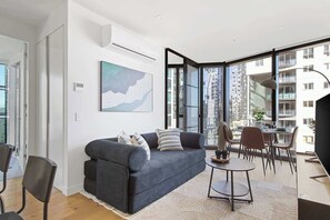 A modern living room with a sofa, chairs, a coffee table, and a dining area with a table and chairs. - Luxury CBD Stay, Pool, Spa & City Views (Melbourne)