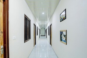 A corridor with doors on both sides, a tiled floor, and framed artwork on the walls. - Suite Lucknow Inn (Lucknow)