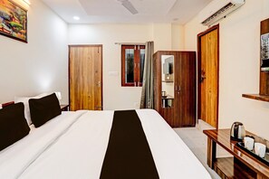 A hotel room with a bed, a wardrobe, a mirror, a television, and a kettle on the side table. - Suite Lucknow Inn (Lucknow)