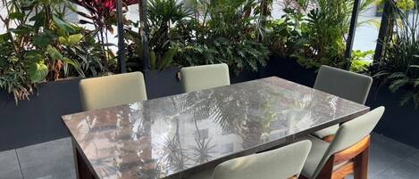 Una mesa rectangular de comedor con superficie reflectante, rodeada por cuatro sillas con asientos acolchados y patas de madera.