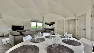 A dining area with a round table, white chairs, and a sofa in the background.